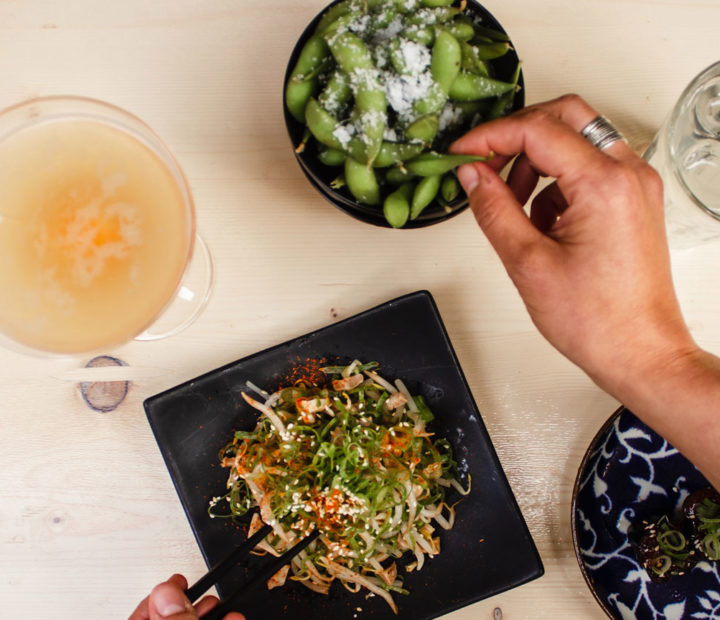 Vegan dishes including edamame beans served on black plates, alongside drinks.